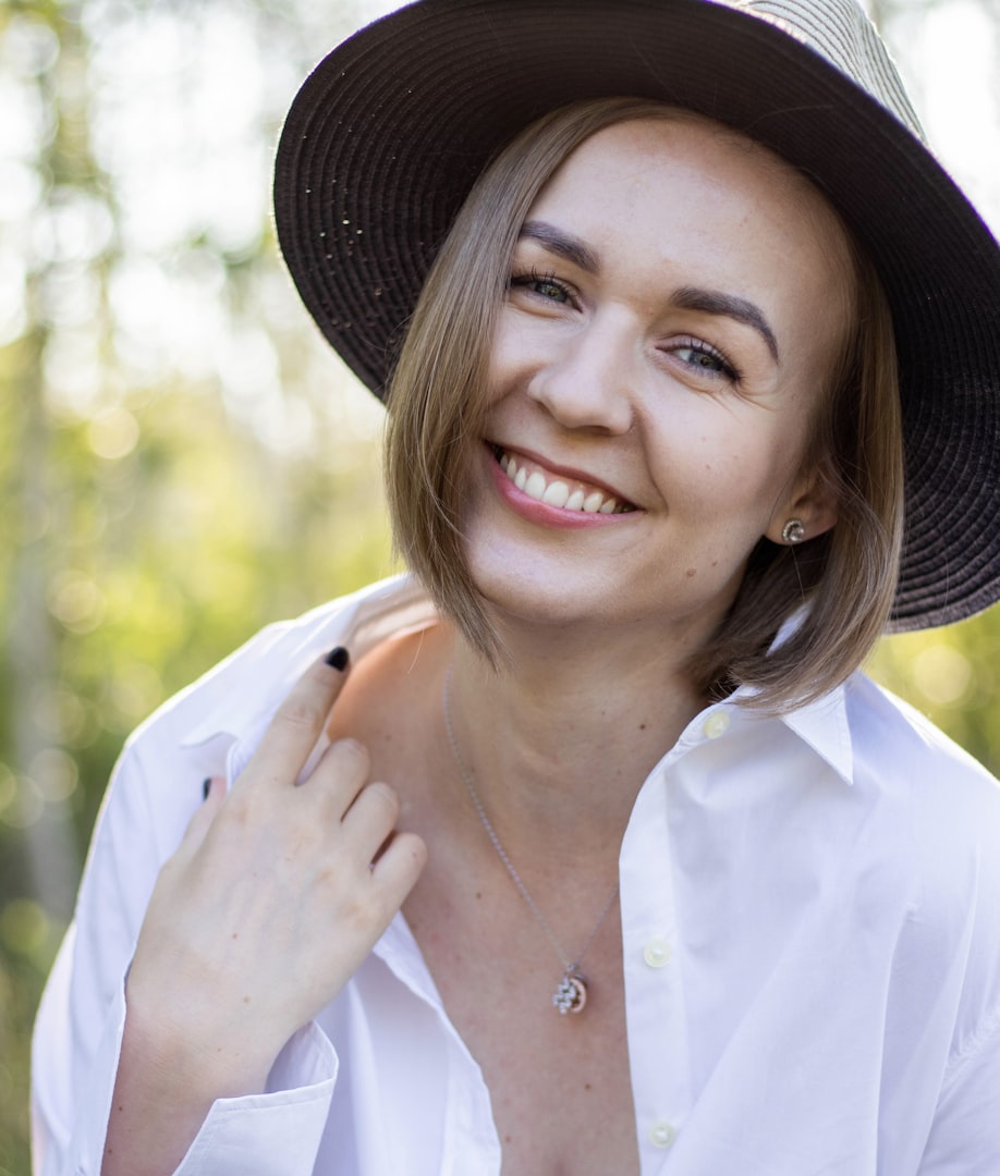 A woman with a confident smile, wearing a white shirt with rolled-up sleeves, stands with her arms crossed against a light gray background.